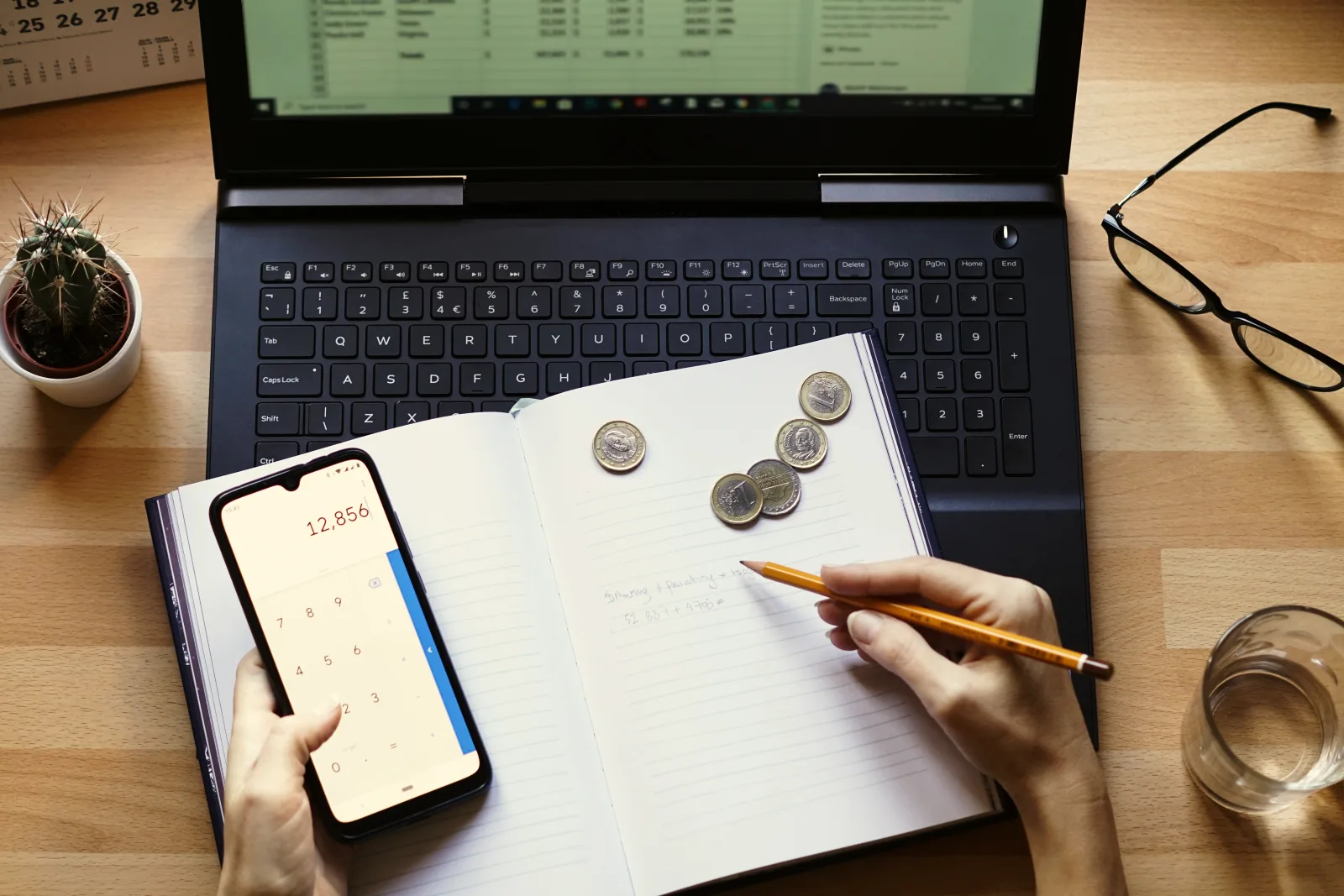Persona calcula un presupuesto con el teléfono, monedas y una libreta